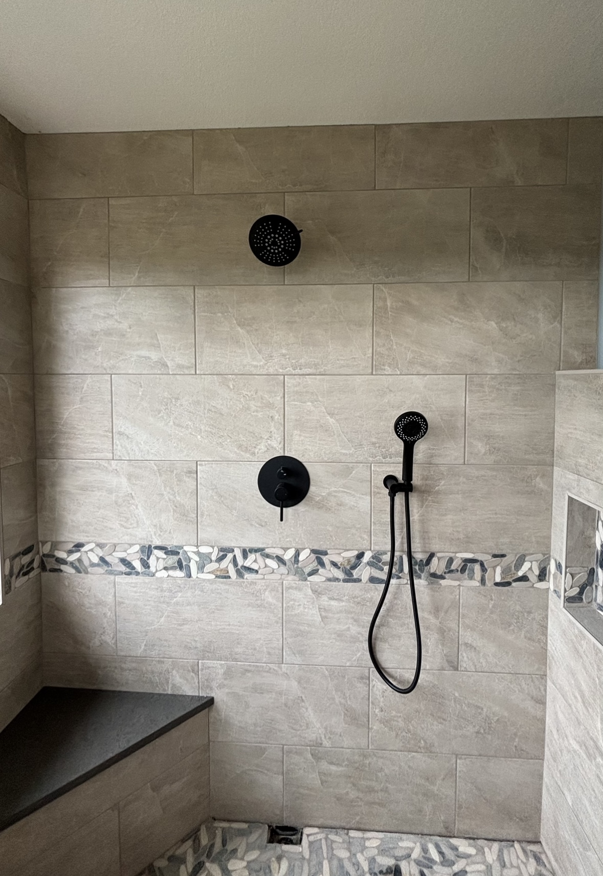 A modern tiled shower with a built-in bench, a wall-mounted showerhead, a handheld shower, and a decorative mosaic tile accent strip.